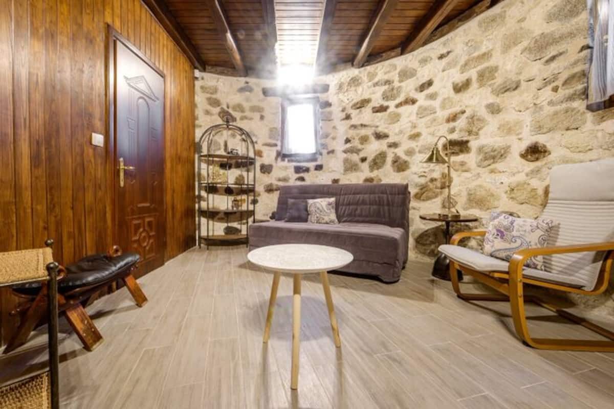 Ground-floor living room with sofa, stone walls and wooden ceiling